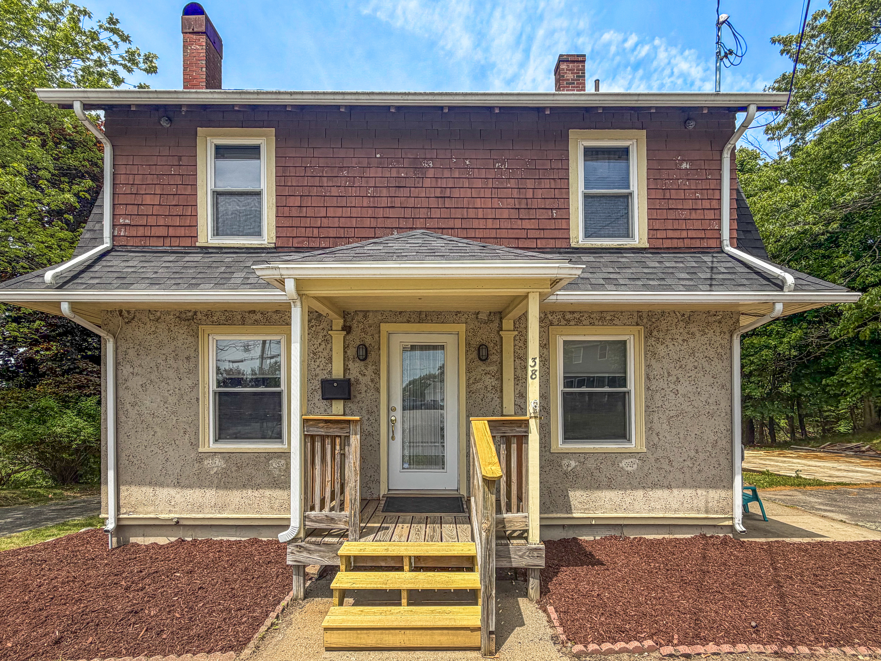 A closer look at the covered porch shows the prominent address markers for simple identification upon arrival. This symmetrical facade highlights the home's unique textures, guiding you toward the side entry path where your vacation begins.