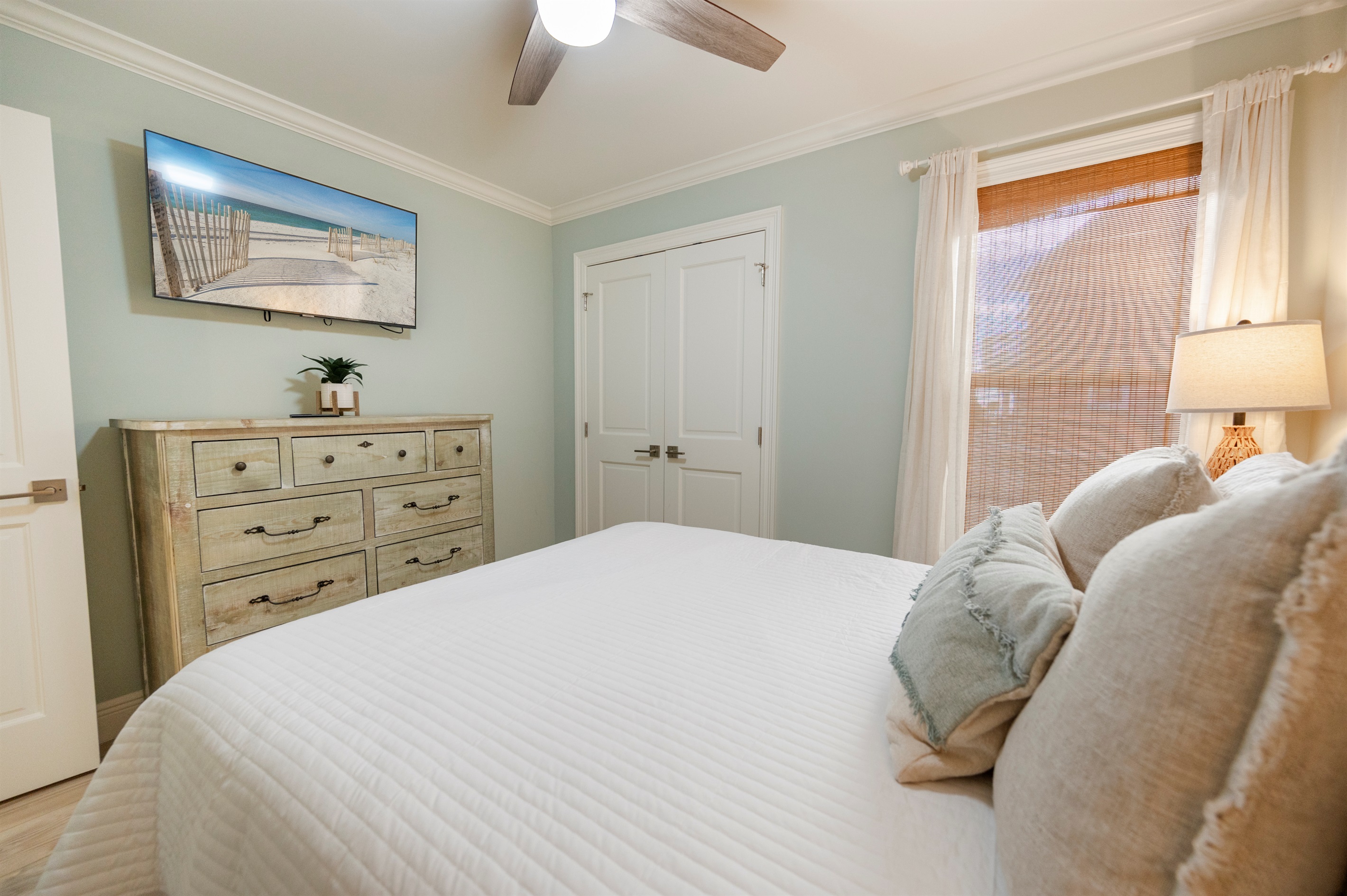 Relax in a cozy beach-inspired bedroom with white bedding, a rustic dresser, warm vibes, and soothing decor.
