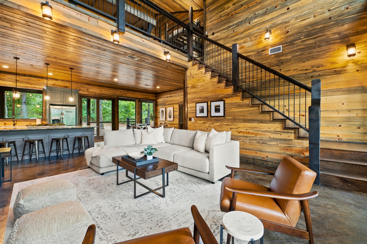 This open-concept living space, with its comfortable seating and chic decor, seamlessly connects to the kitchen and features a loft overhead, creating a perfect gathering spot for guests.