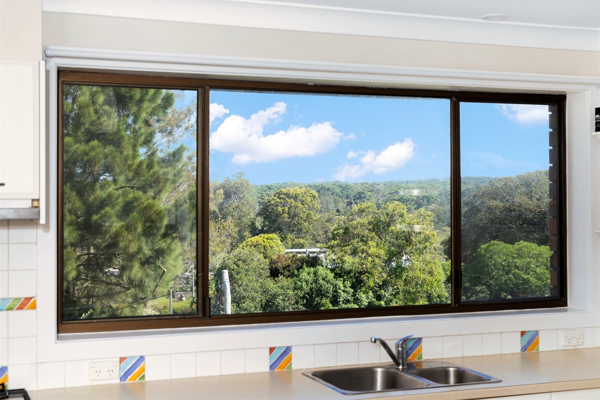The upstairs kitchen at Bertie’s 3 Beaches Moruya Heads looks across leafy treetops, adding a coastal-bush outlook to the main living level.