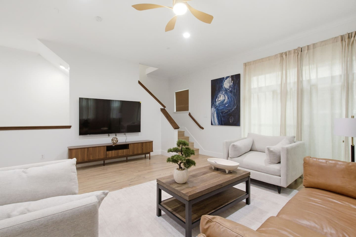 Smart TV, spacious sectional seating, and a clean sightline through to the kitchen and staircase. The kind of living room that actually fits a full group comfortably.

