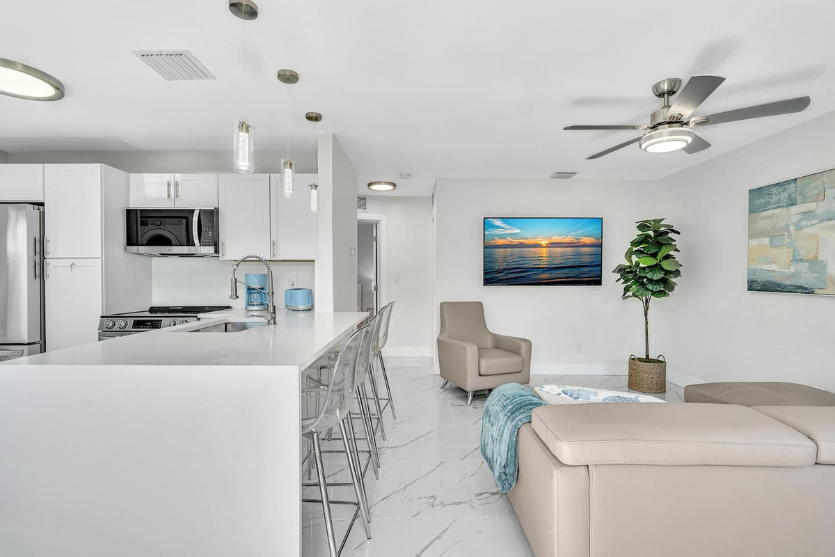Open-concept living room and kitchen with comfortable seating, a large TV, breakfast-bar seating, and a fully equipped kitchen with stainless steel LG appliances.