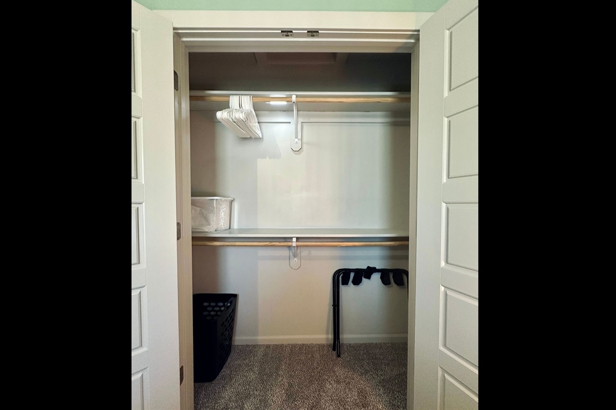 Queen bedroom closet thoughtfully equipped with hangers, luggage rack, extra linens, and laundry basket for a comfortable stay.