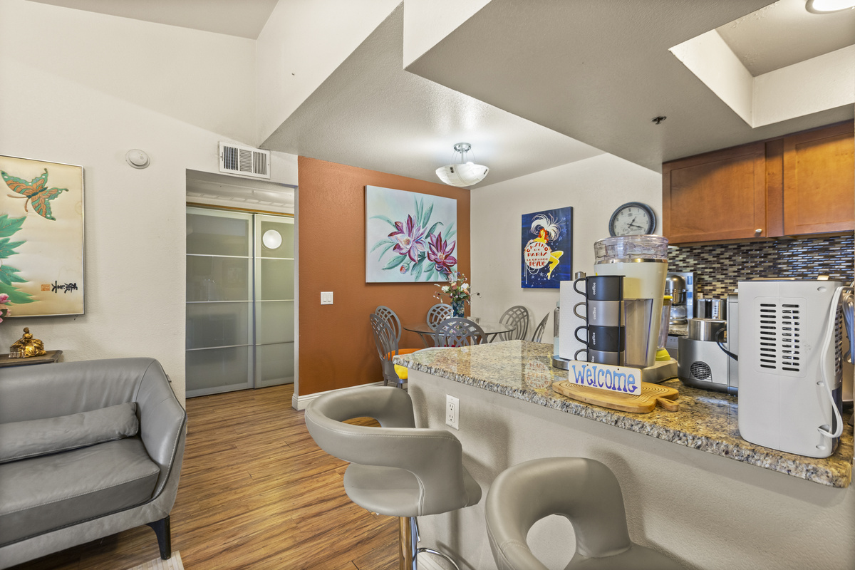 Kitchen bar with two stools, drink station, and the dining and living spaces connected nearby.
