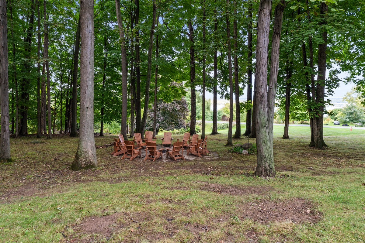 Gather around the fire pit under towering trees, complete with Adirondack chairs and a serene view of the lake in the distance.