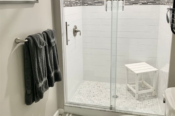 Refresh in our clean, updated bathroom featuring a spacious walk-in glass shower with sleek white subway tile and a decorative mosaic border. The shower is equipped with a convenient seat and plush charcoal towels for your comfort.
