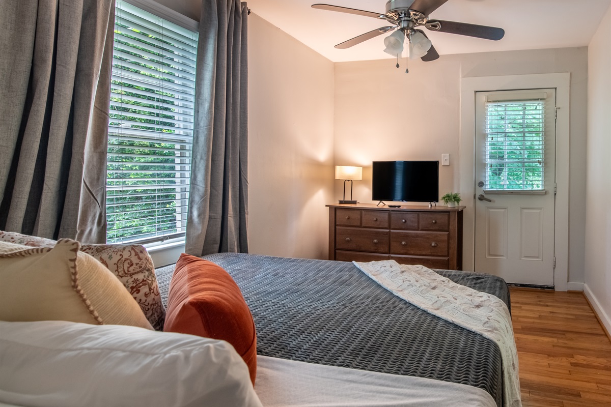 Bright bedroom with large windows, a ceiling fan, and TV — offering comfort and convenience.