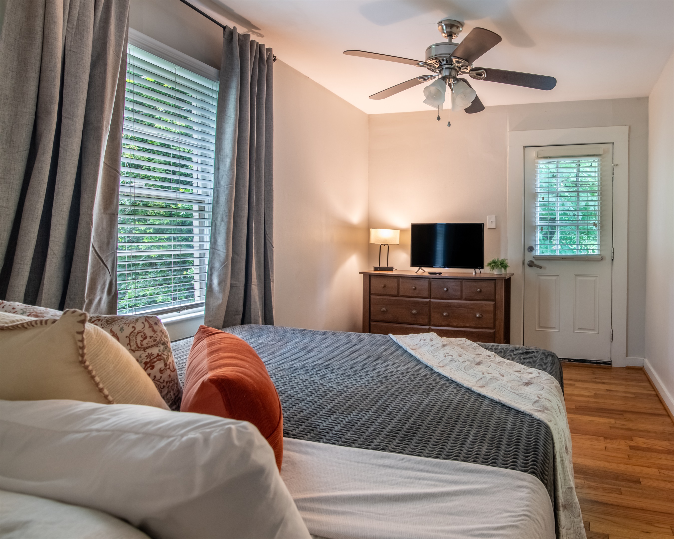 Bright bedroom with large windows, a ceiling fan, and TV — offering comfort and convenience.
