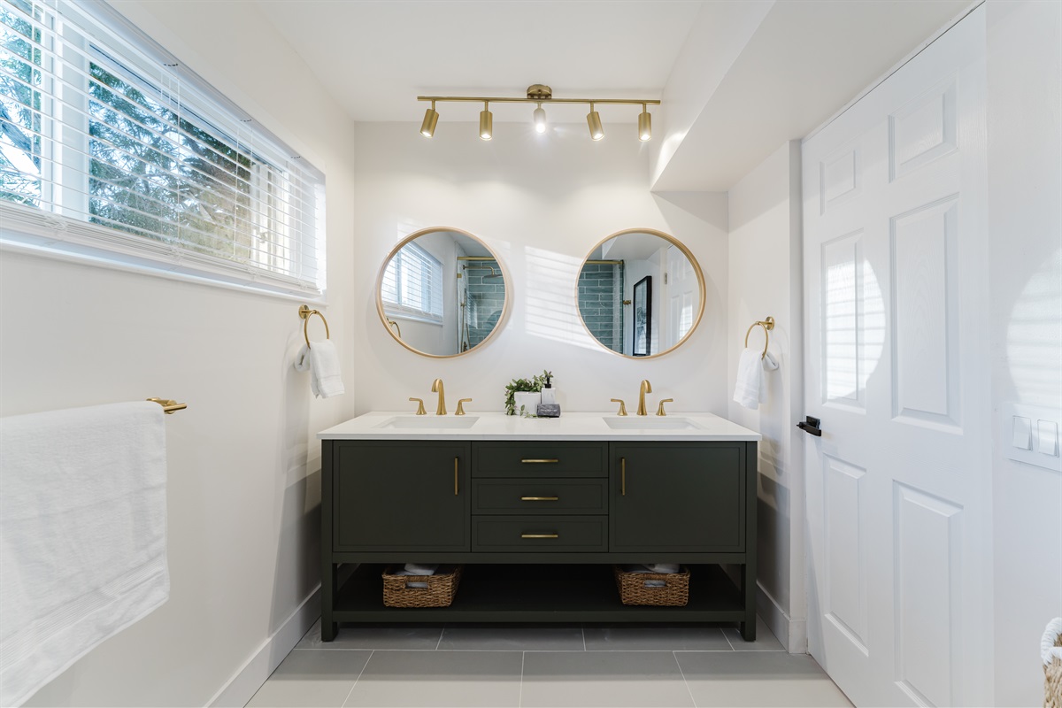 Spa-inspired ensuite with a walk-in glass shower, soft sage tile, and brushed brass fixtures. A double vanity with designer mirrors creates a bright, hotel-style retreat made for slow mornings and effortless luxury.