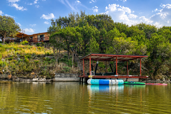 Private lakefront dock stocked for fun on the water, with life jackets, an inflatable trampoline, lily pad, inflatable kayak, canoe, and assorted inflatable tubes.
