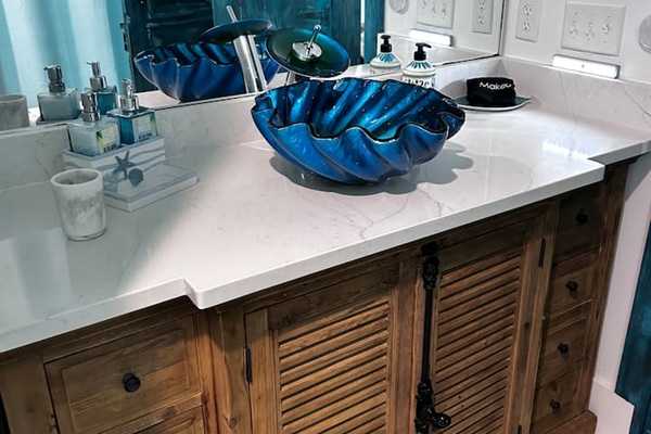 Artisan Charm: One-of-a-kind antique cabinet with industrial bolt detailing, topped with a whimsical shell sink. A custom touch of coastal elegance in the main bath.