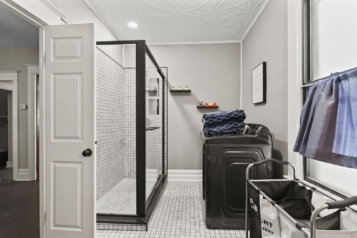 Modern bathroom featuring a sleek shower with a glass door cover, an automatic washing machine, elegant wall design, and polished flooring—combining functionality with sophisticated style for a luxurious feel