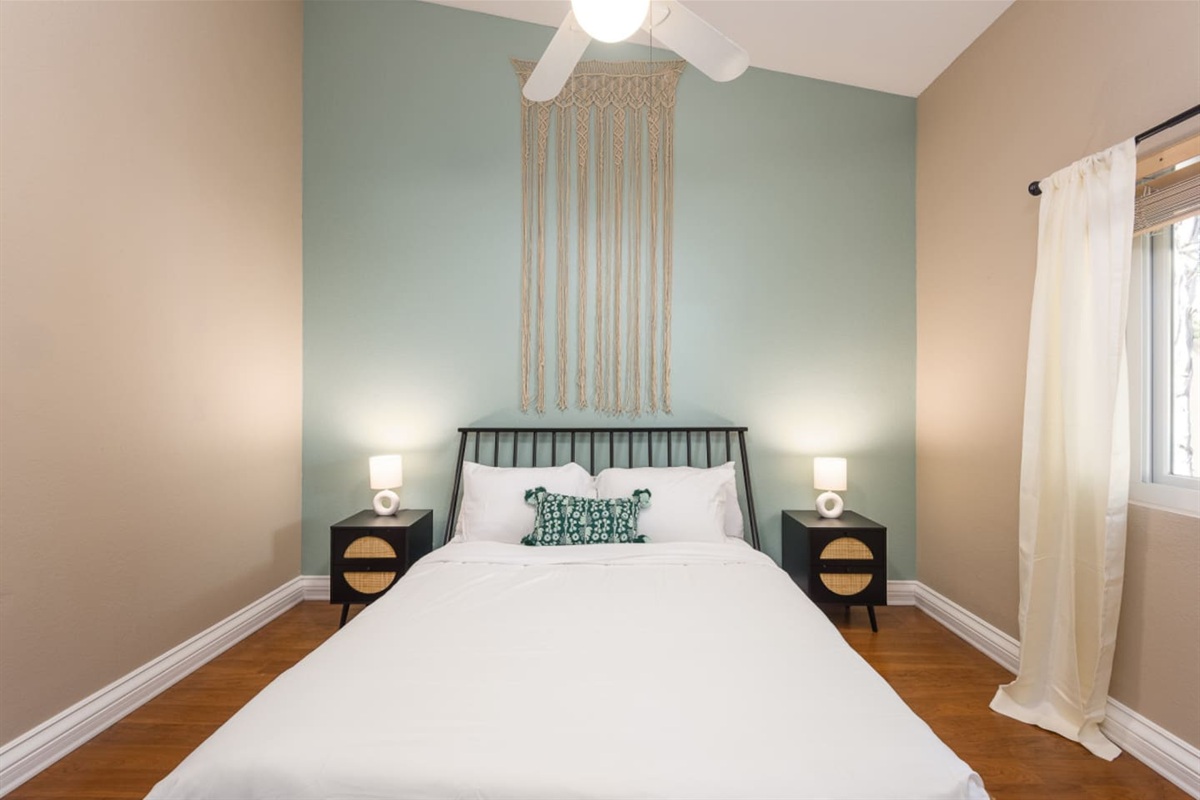 Guest bedroom with a queen bed, ceiling fan, bedside lighting, and a calm accent wall for a restful stay.