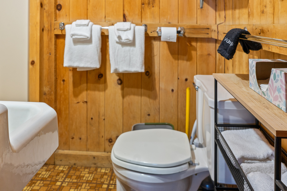 Camp bathroom setup at Loonrise Point! Features fresh plush towels, dedicated makeup washcloths, storage cart, toilet, and sink with classic pine walling. Clean and practical amenities on Beech Hill Pond in Otis, ME.