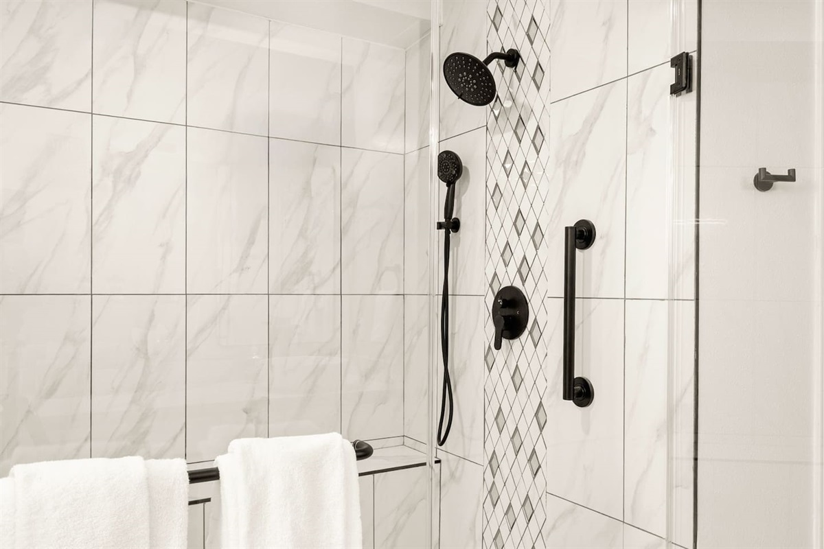 Sleek glass walk-in shower with marble-style tile, matte black fixtures, rainfall showerhead, and safety grab bar—clean, modern, and perfect for a relaxing spa-like rinse after a long day.
