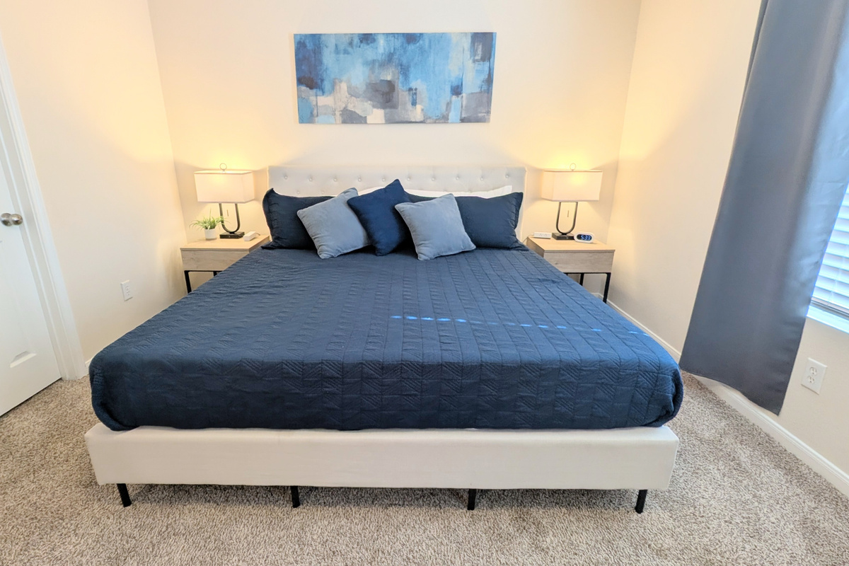 Oversized Primary suite includes a large walk-in closet, ceiling fan, cozy bedding, blackout curtains, a Roku TV, and dedicated workspace. Bedside tables have storage, an alarm clock, and easy access to charging ports.