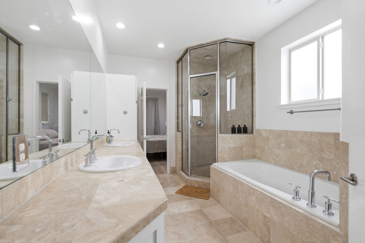 Primary en-suite bathroom with soaking tub, walk-in glass shower, double vanity, and generous counter space. Stocked with Ginger Lily Farms bath essentials for your arrival.

