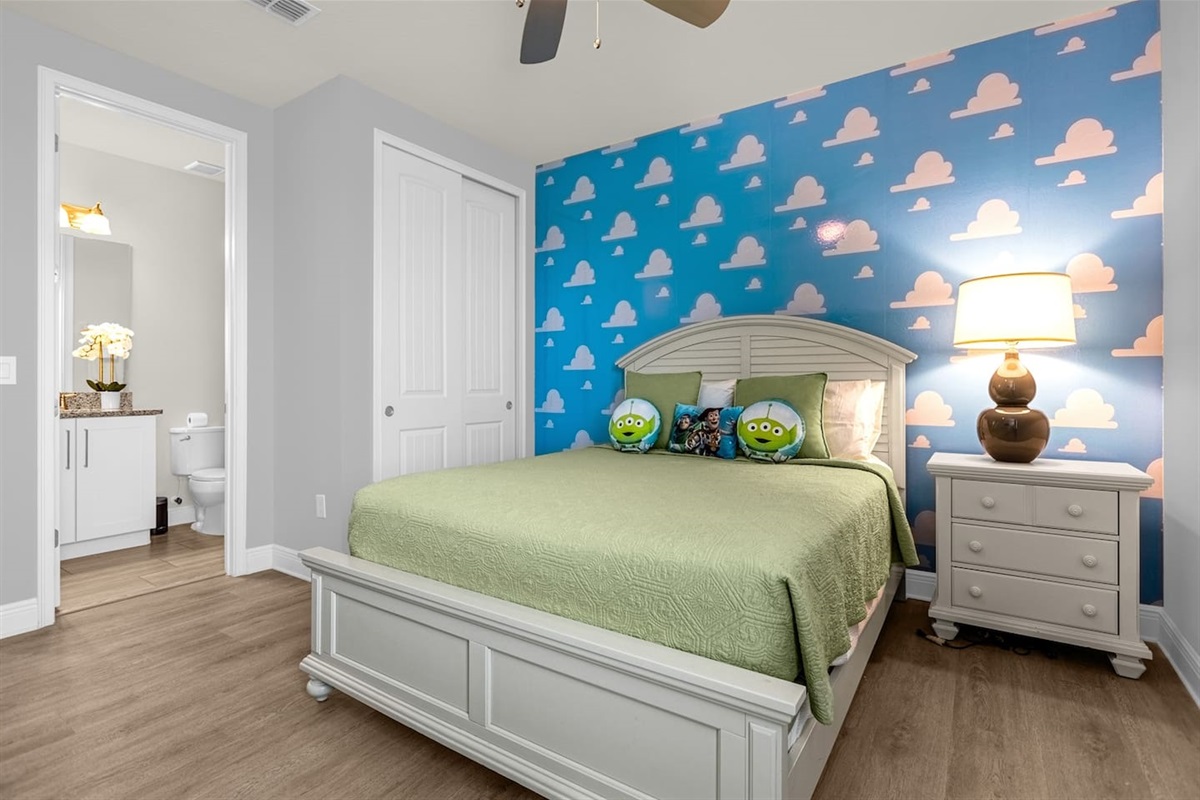 The room is a playful homage to the beloved "Toy Story" franchise, bursting with bright colors and nostalgic decor. The walls are painted a soft sky blue, adorned with large, cartoonish clouds reminiscent of the iconic wallpaper from Andy’s room.