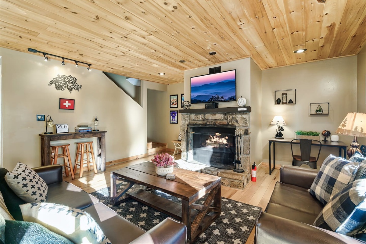 The main living room area features a real wood-burning fireplace, smart TV, comfortable lounge area, a pull-out sofa bed, and a desk work space. Walk out to the covered porch with hot tub.