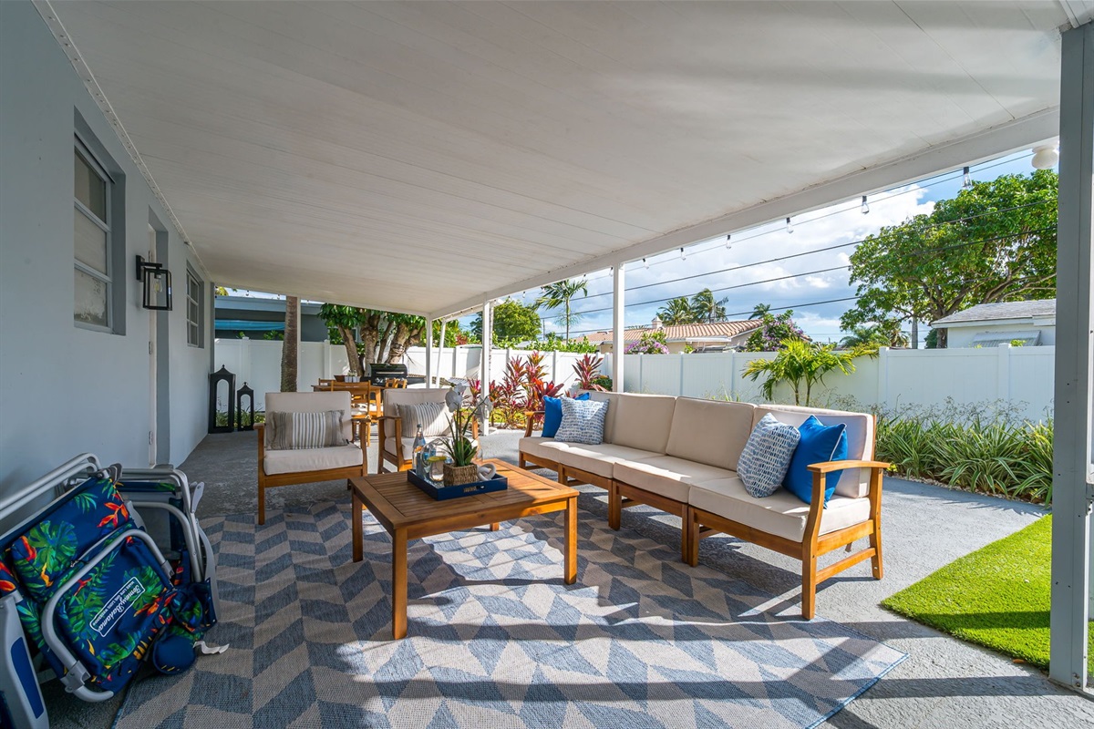 A serene covered patio with chic seating, alfresco dining, a gas grill, and a two-person hammock, all framed by a mix of manicured turf and lush lawn—your private outdoor retreat.