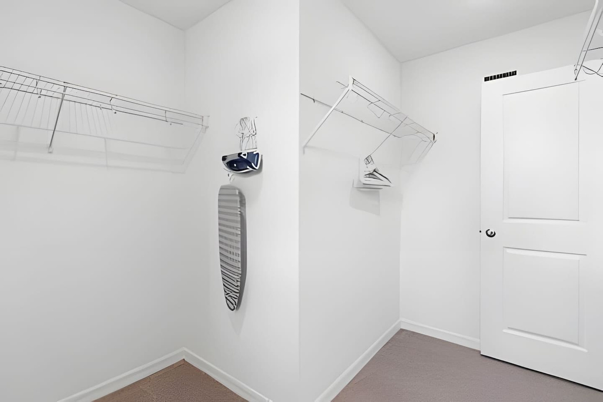 Spacious walk-in closet featuring hangers, an ironing board, and iron.
