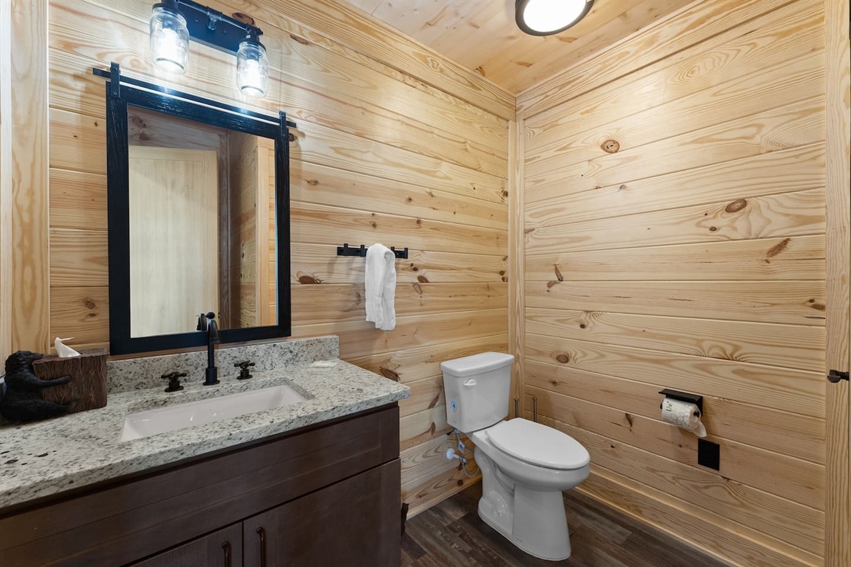 Rustic charm meets functionality in this stylish half bath, featuring a granite countertop, wood-paneled walls, and modern black fixtures.