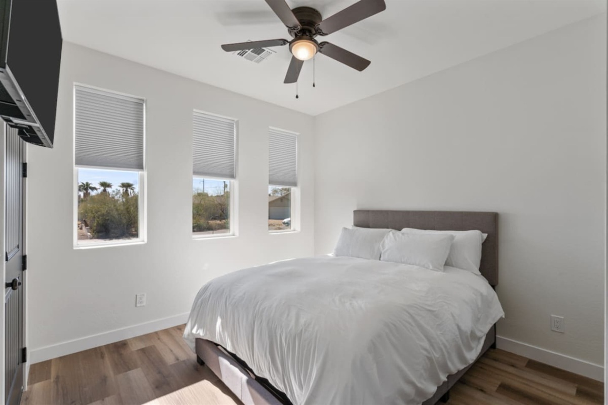 Bright guest bedroom with a comfortable bed, wall-mounted TV, and plenty of natural light.