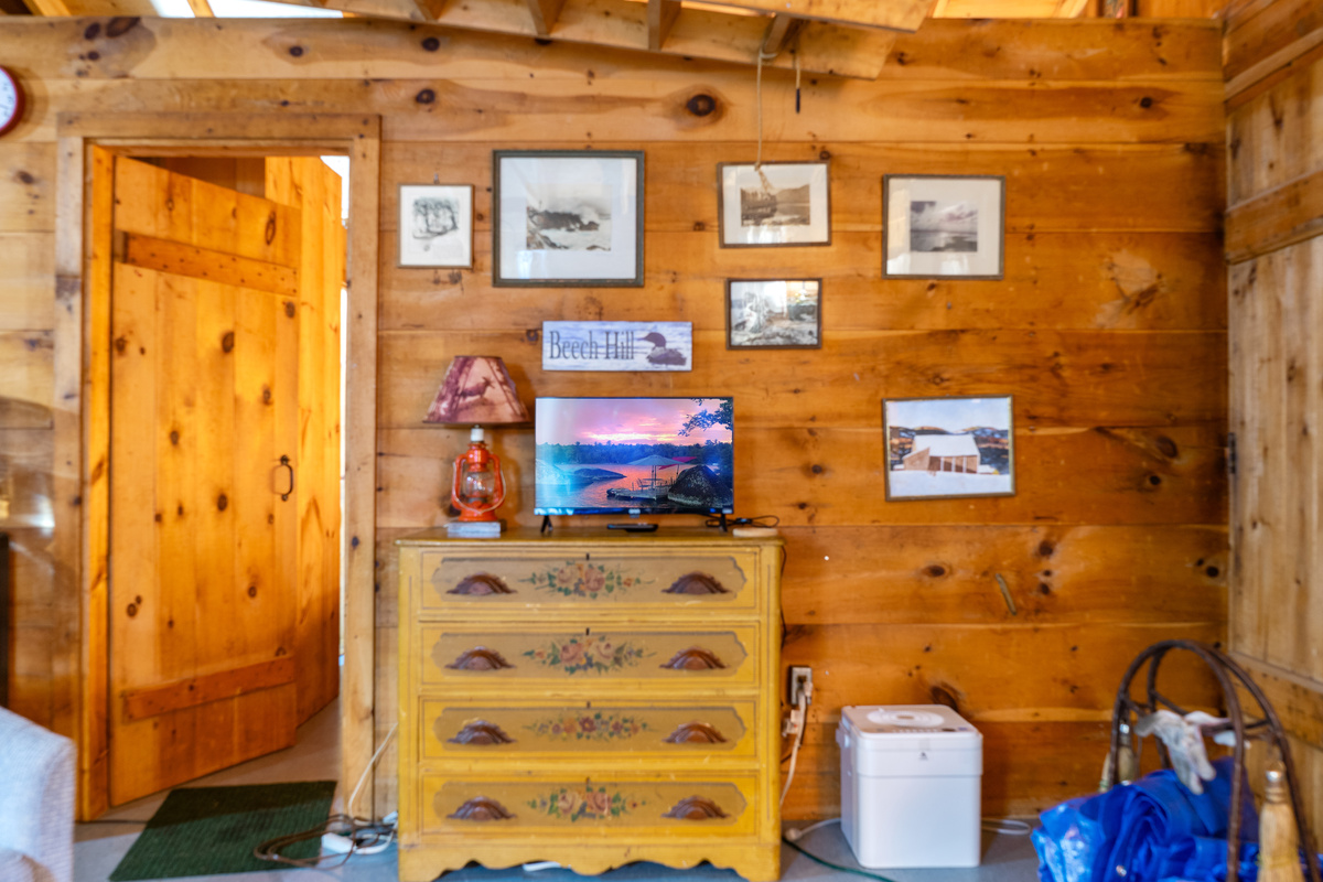 Smart TV station at Loonrise Point! Small Smart TV sits on a vintage dresser, perfect for streaming your favorite shows. Surrounded by knotty pine walls and framed lake art, blending modern entertainment with rustic camp style in Otis, ME.