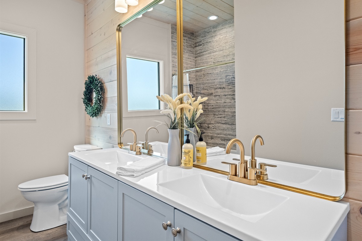 Bathroom with stylish gold fixtures, dual sinks, and shower-tub combo.