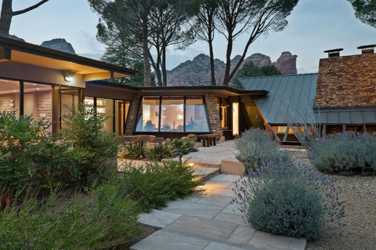 Architectural focal point with dramatic angled windows, stone accents, and mountain views framed by lush greenery.