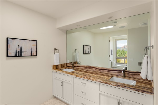 Even the vanity comes with a view! Freshen up in this bright, luxurious bathroom featuring striking stone details and a massive mirror that perfectly catches the reflection of the Sedona red rocks.