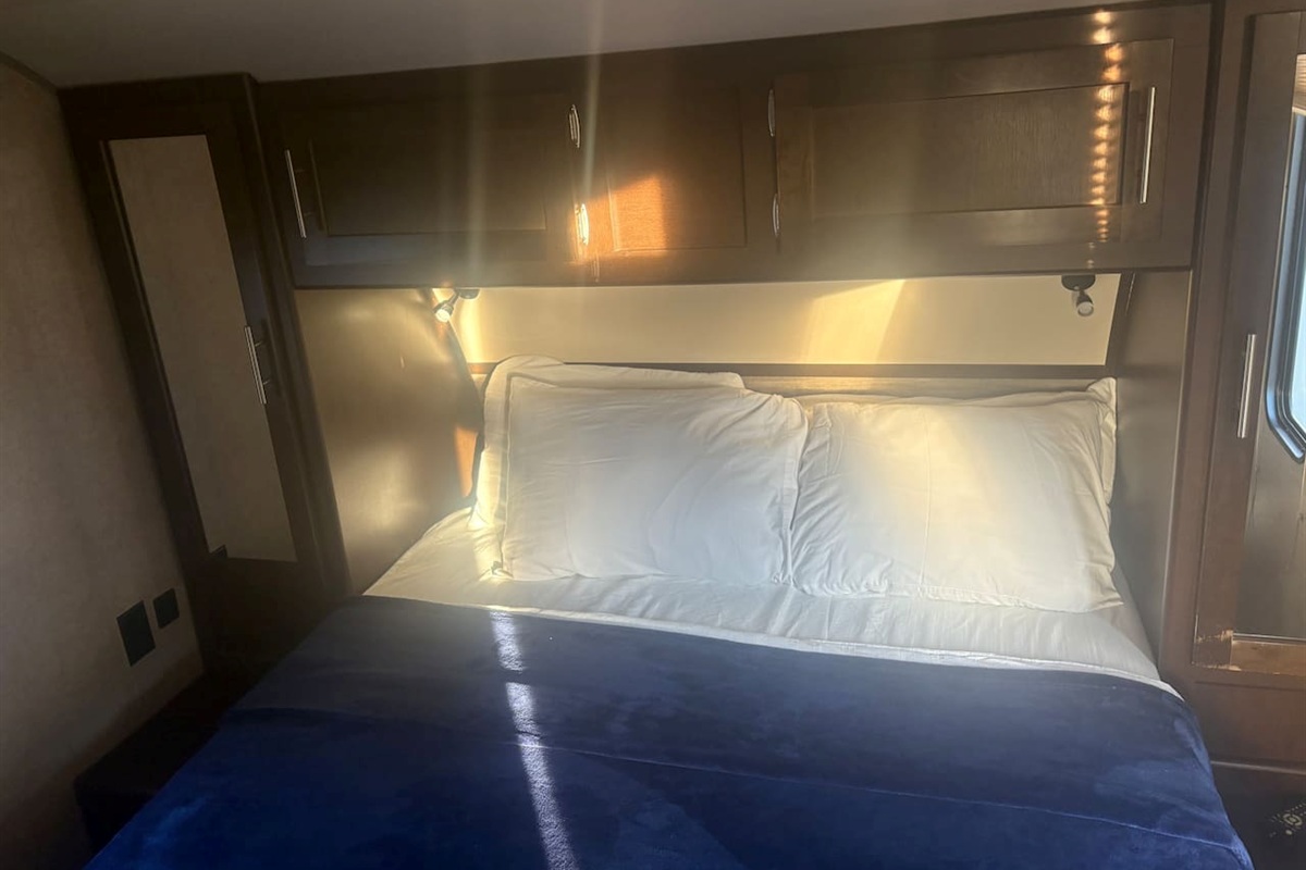 Queen size bed with four pillows. Bathroom towels are stored in the cabinet above bed.