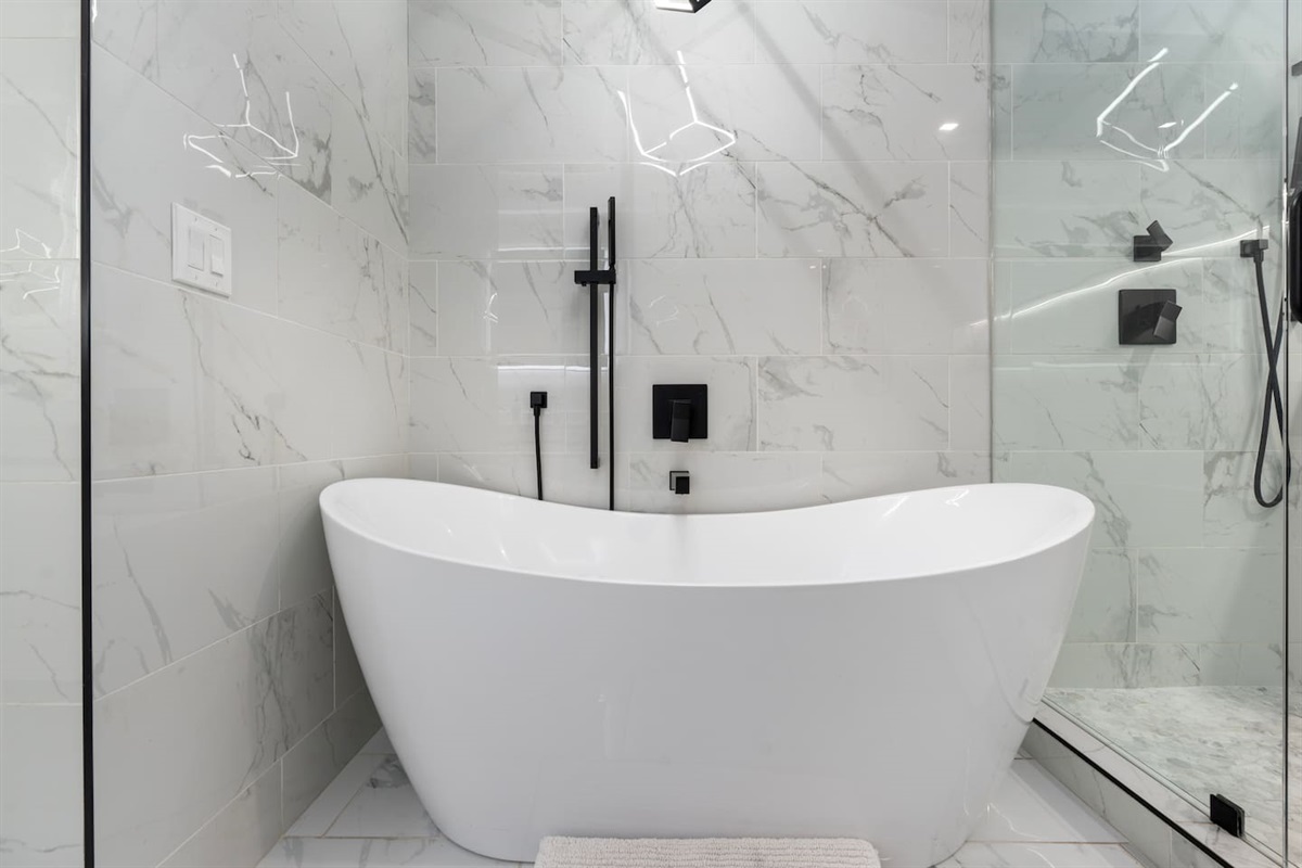 Freestanding tub surrounded by sleek marble tile and matte black fixtures.

