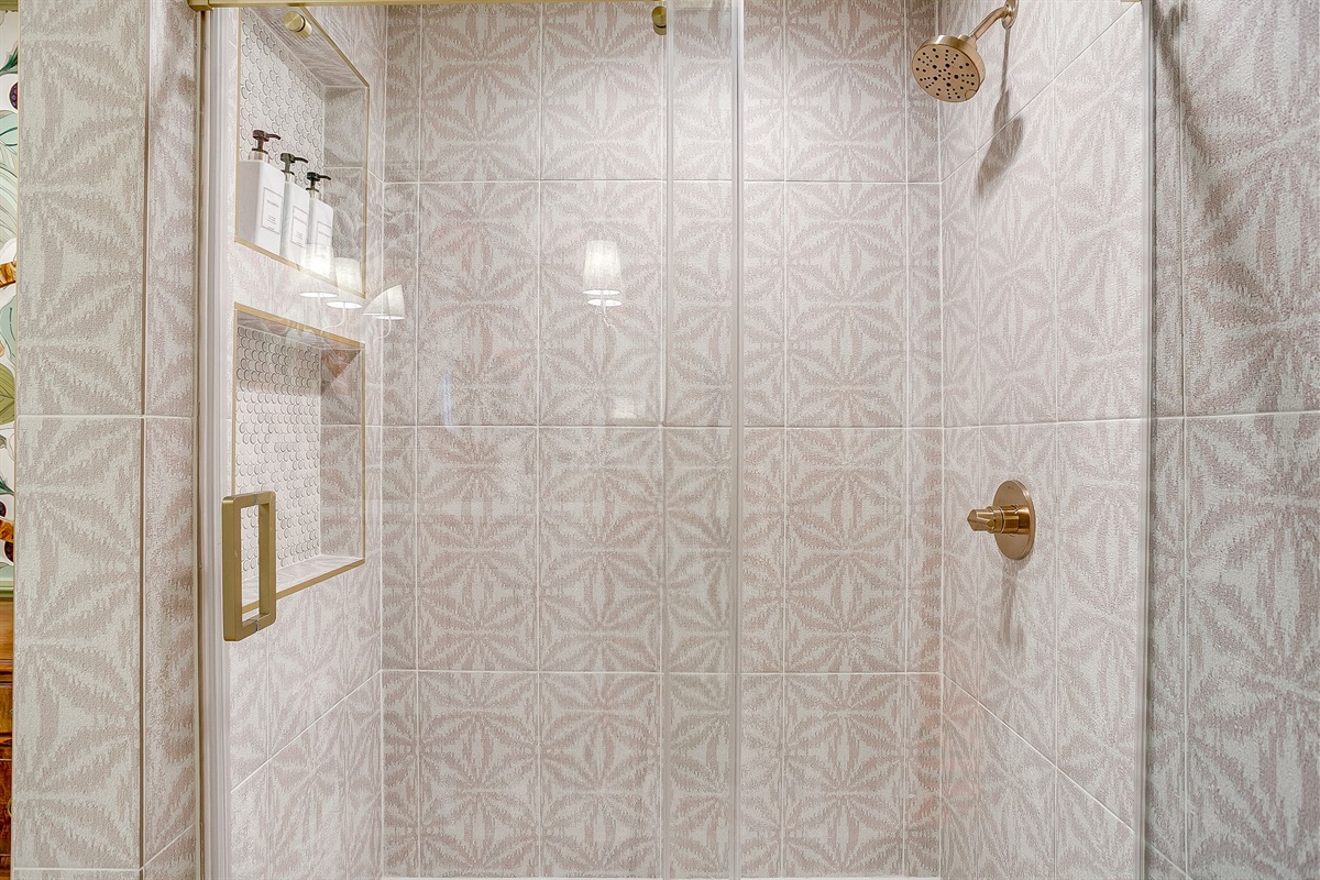 Rear bath shower with playful tile, built-in niches stocked with shampoo, conditioner, and body wash, and a sleek glass barn door finished in warm gold hardware.