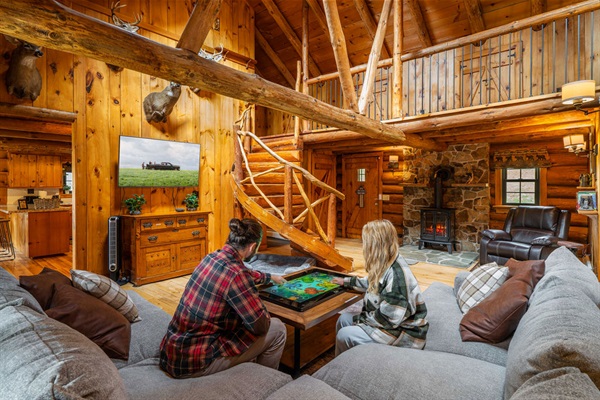Gather around the Infinity Game Table in the cozy log cabin living room, complete with stone fireplace and rustic charm.