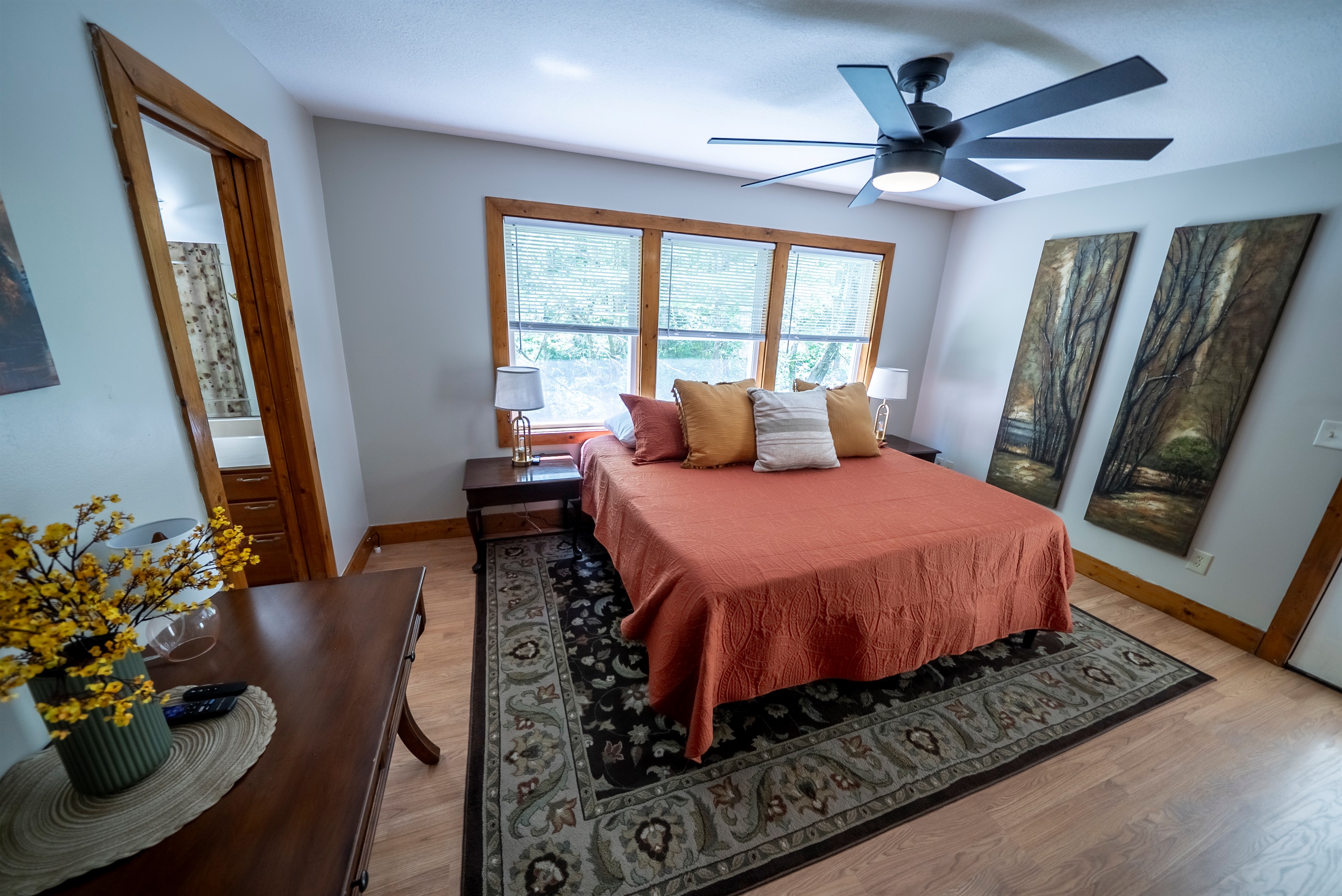 Spacious primary suite with a king bed, large windows overlooking the creek, direct access to the deck, Smart TV, ceiling fan, ample closet space, and private en suite.
