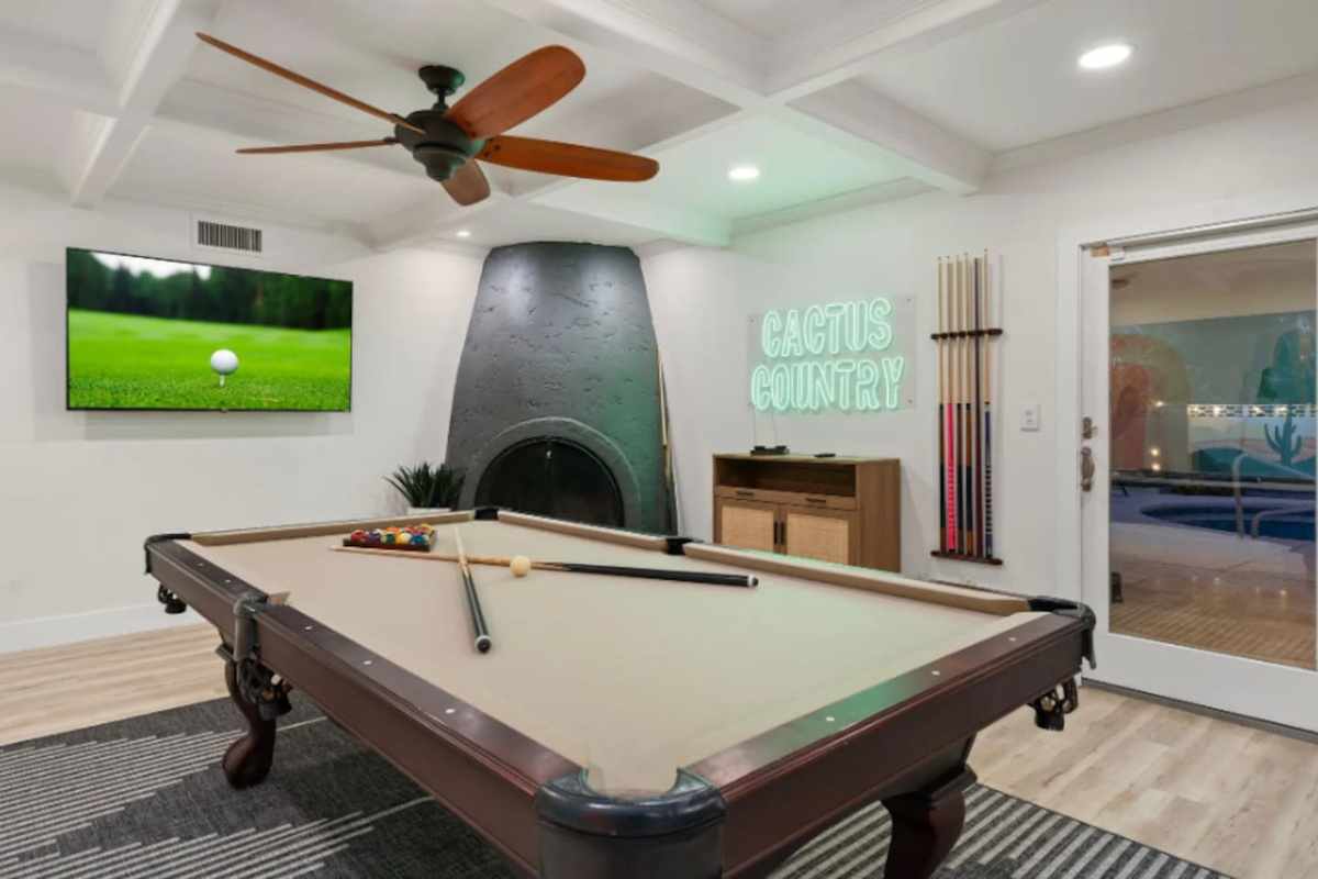 A stone fireplace adds warmth to game nights, with the pool table and neon signage making this room feel like a private lounge.
