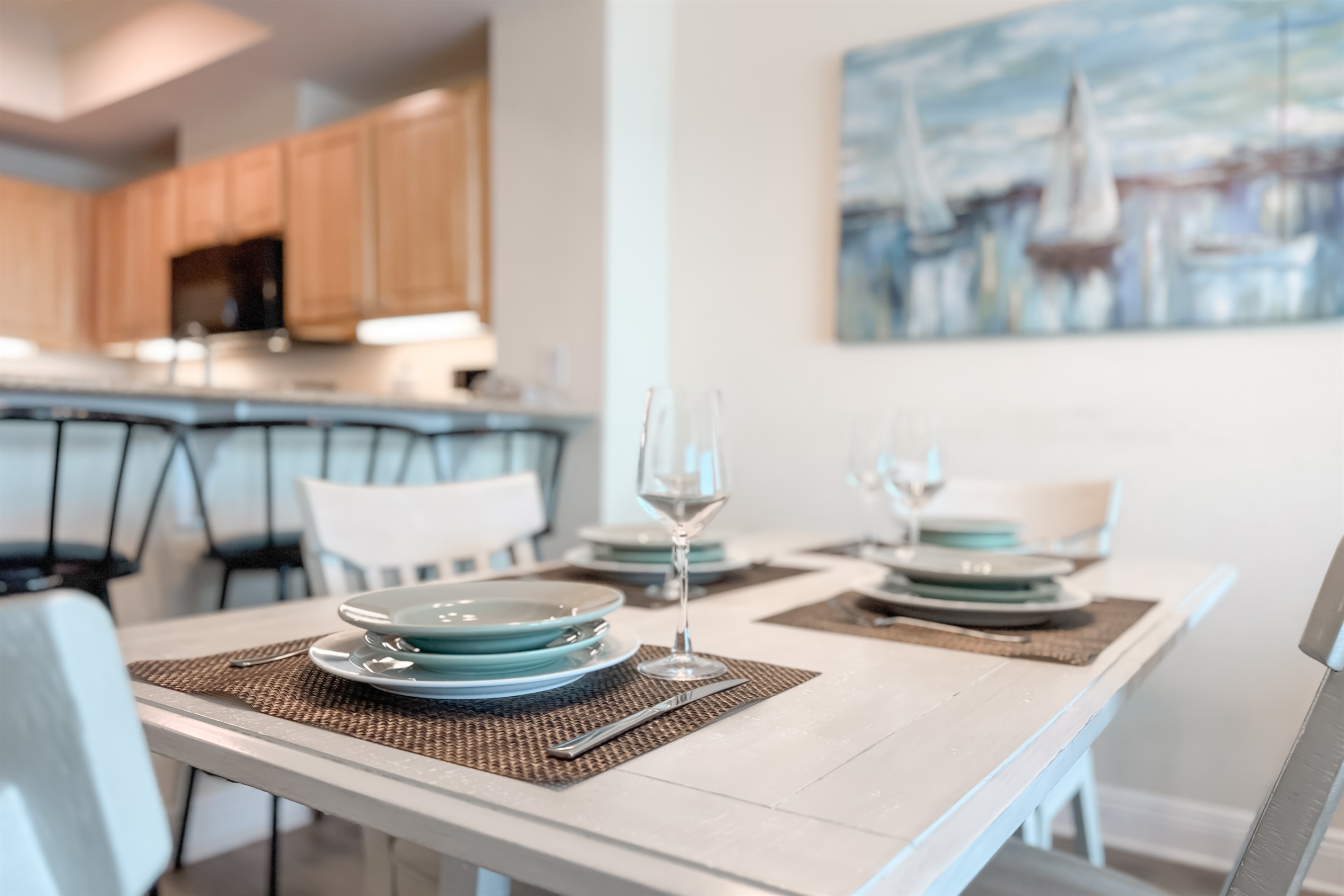 Gather around the beautifully appointed dining table, where every detail, from the textured placemats to the delicate glassware and serene colored plates, creates an inviting atmosphere for memorable meals.