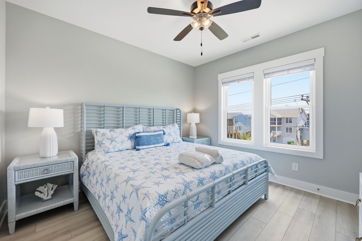 A serene king bedroom features plush bedding, coastal-inspired d&eacute;cor, a Smart TV, and plenty of natural light for a relaxing retreat