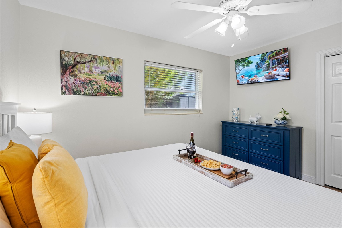Unwind in this cheerful bedroom featuring crisp white linens, golden accent pillows, and tropical garden views through the window.