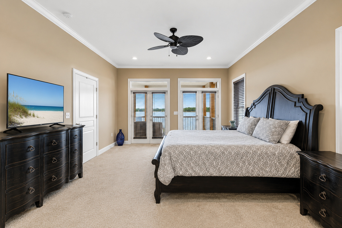Spacious bedroom with dark wood furnishings, smart TV, and private balcony doors framing the lagoon