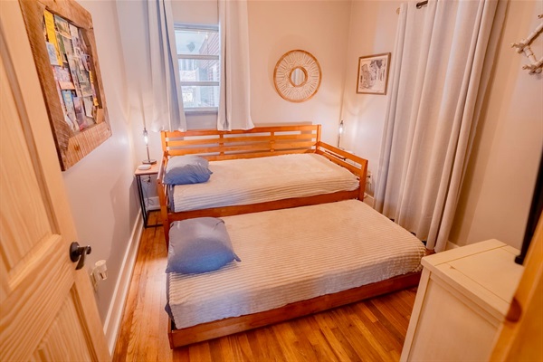 Cozy bedroom with a daybed and trundle, hardwood floors, soft lighting, and simple décor. A comfortable space ideal for kids or additional guests.