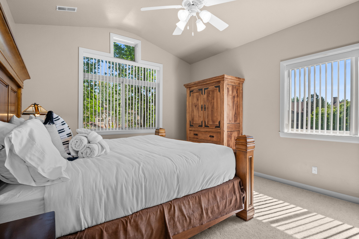 The bright and inviting primary bedroom features vaulted ceilings, large windows with beautiful natural light, and warm wood furnishings for a relaxing mountain retreat atmosphere.