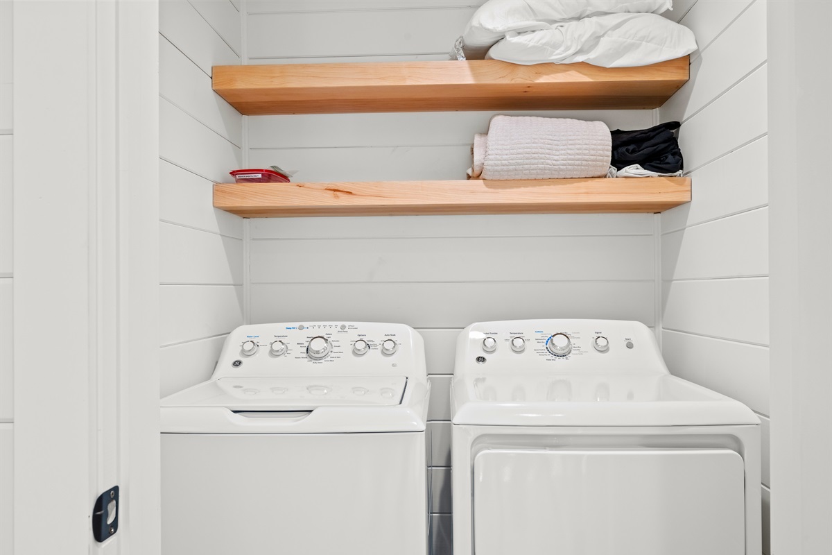 Laundry area with washer, dryer, and open shelving.
