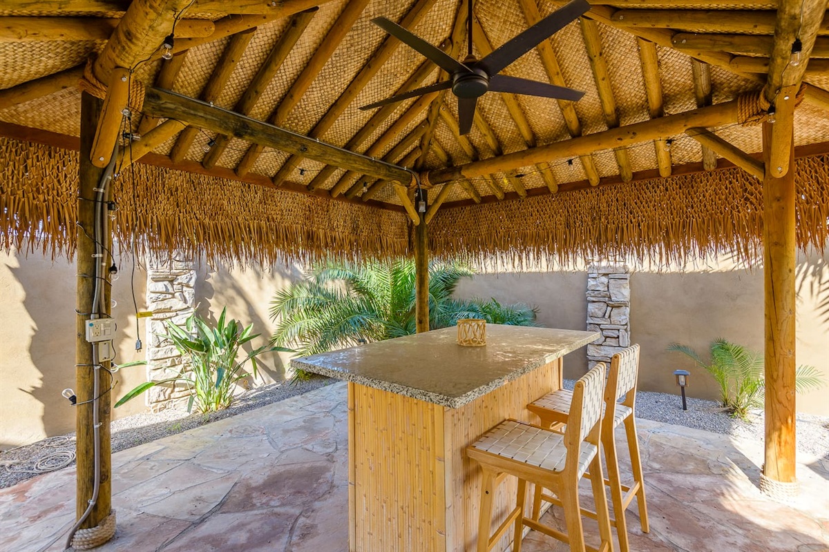Outdoor tiki pergola lounge with bar seating, ceiling fan, and a shaded spot to relax by the pool.
