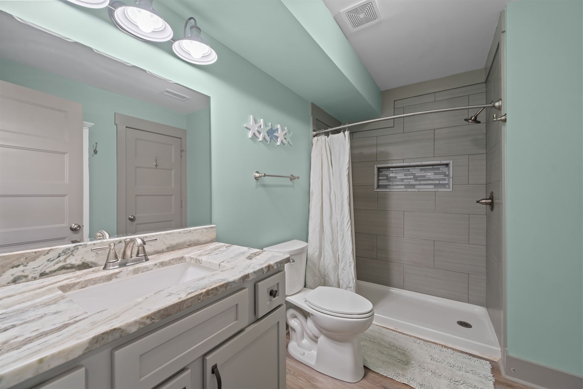 Convenient 1st floor bathroom with a walk-in shower, stone-top vanity, and clean coastal finishes: ideal for guests and easy access from the main living areas