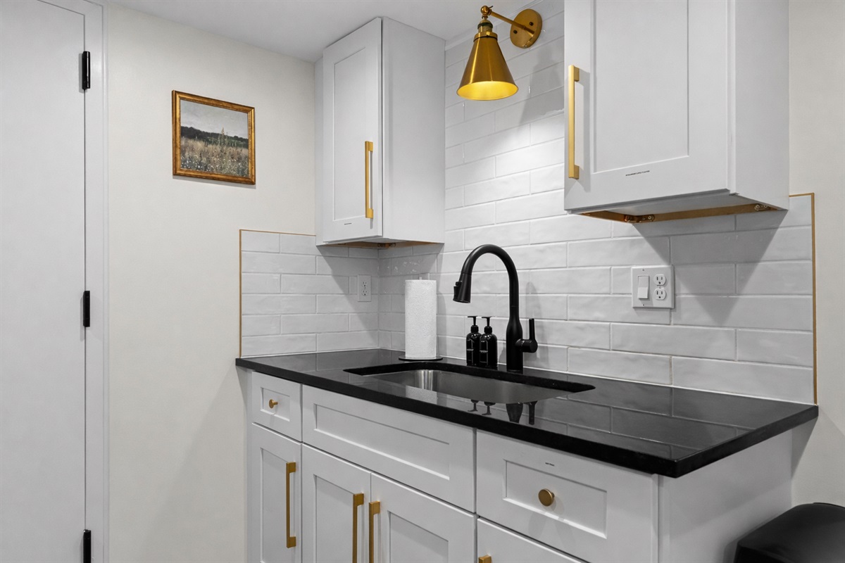 Sleek, modern kitchenette with crisp white cabinetry, bold black countertops, and elegant brass accents—perfect for effortless meals and a polished stay.
