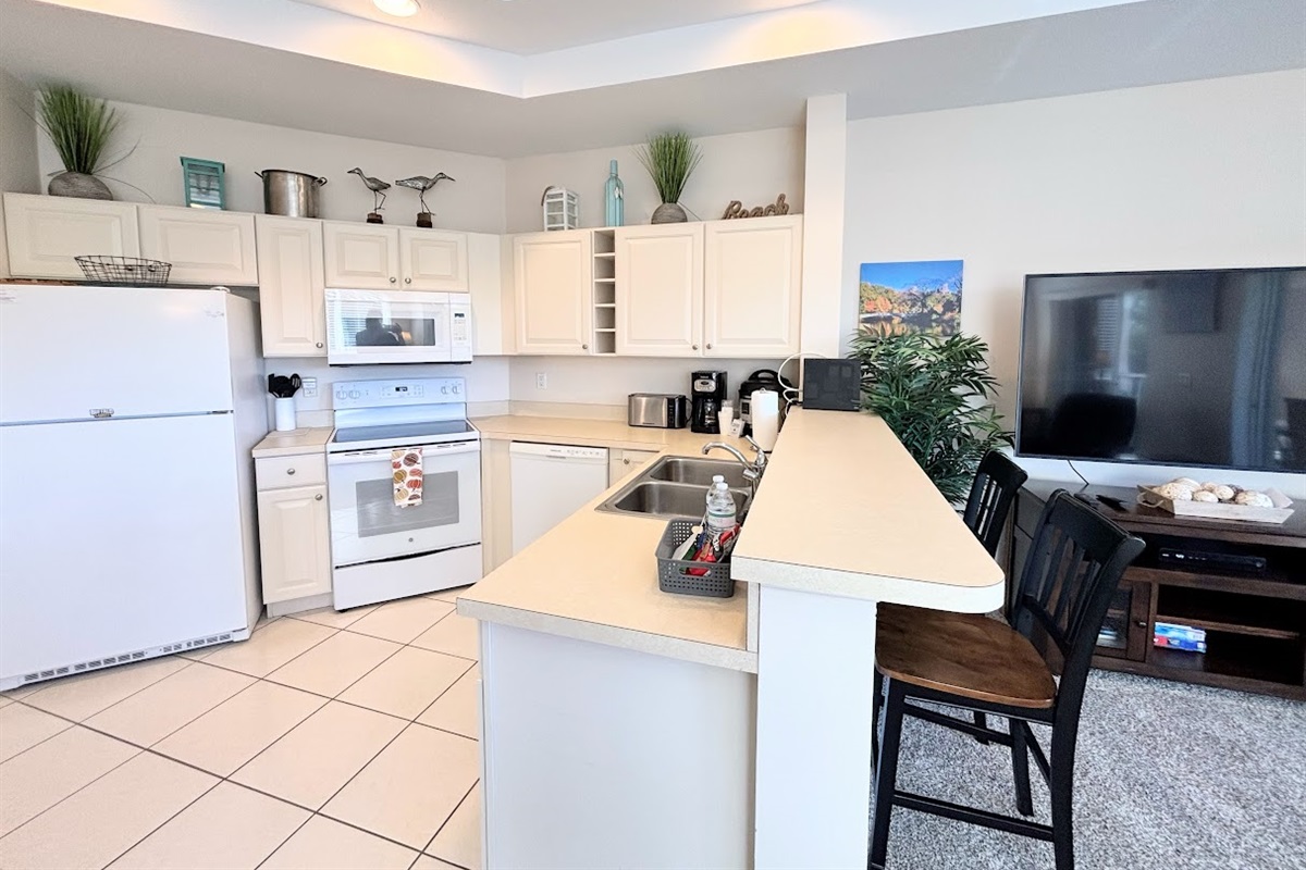 Fully equipped kitchen with full-size appliances, breakfast bar seating, and an open view into the living area.