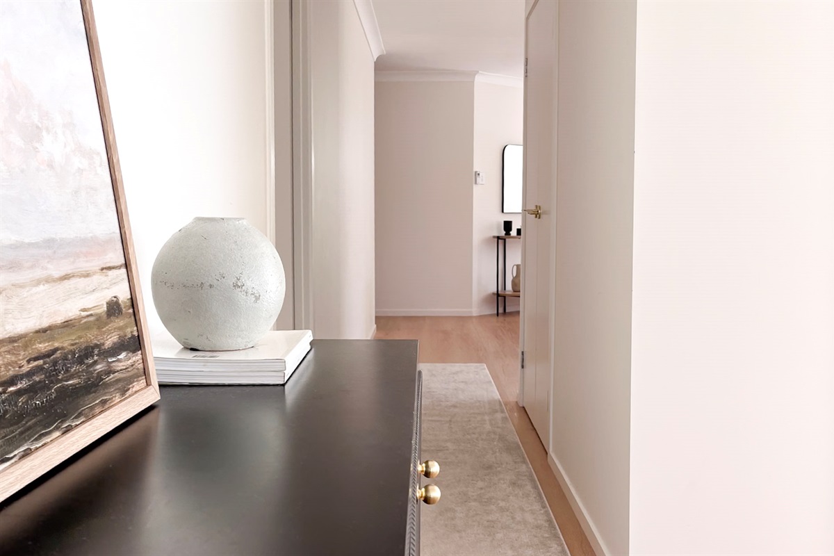 The hallway includes a console, artwork, rug runner and timber flooring, giving the home a clear path between living and bedrooms.