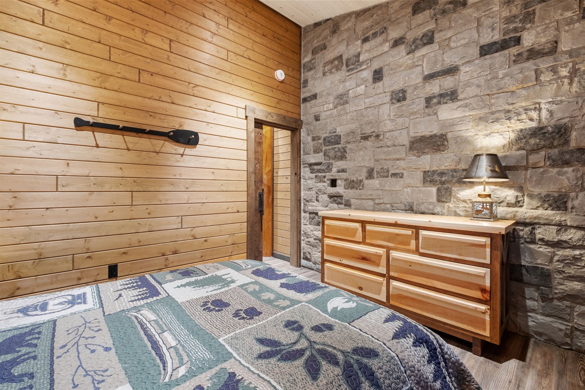 Stylish queen bedroom with a striking stone feature wall, paddle-themed décor, and custom-built wooden dresser — cozy and full of character.